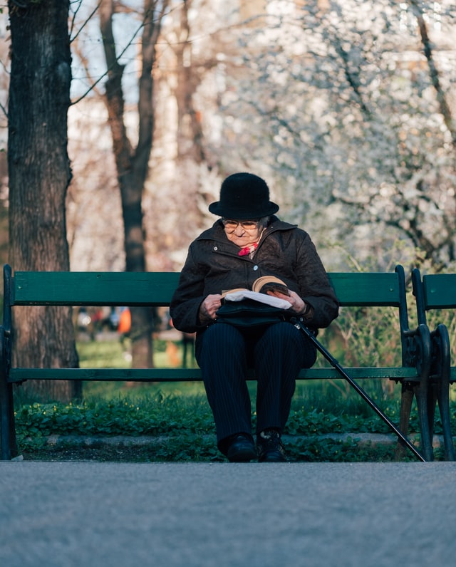 mujer anciana leyendo en un banco de un parque